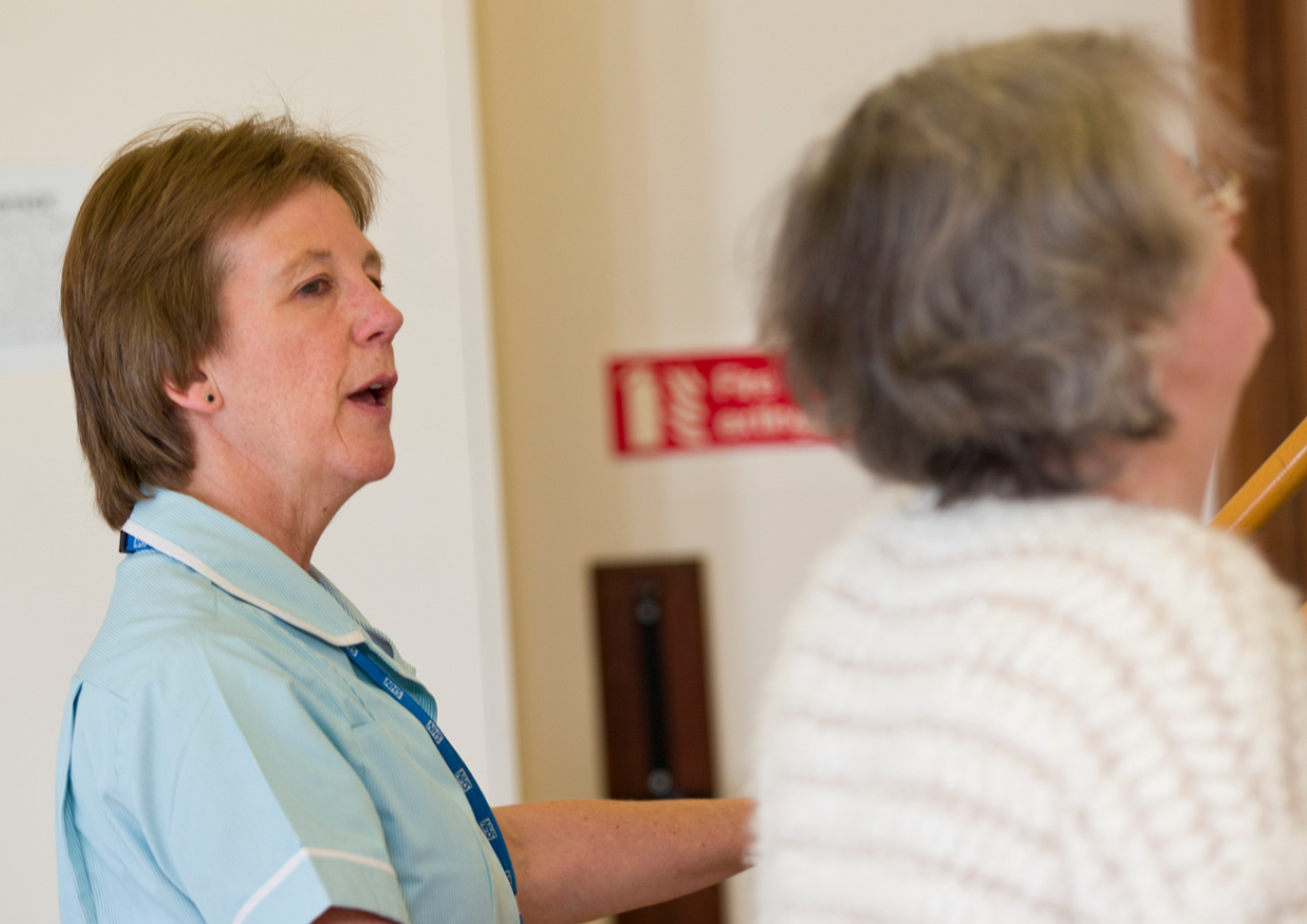 A physiotherapist stands next to an elderly woman who is stretching against gym rehabilitation equipment. 
